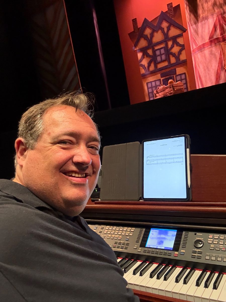 R.J. at the keyboard in the orchestra pit, the Something Rotten! set lit behind him